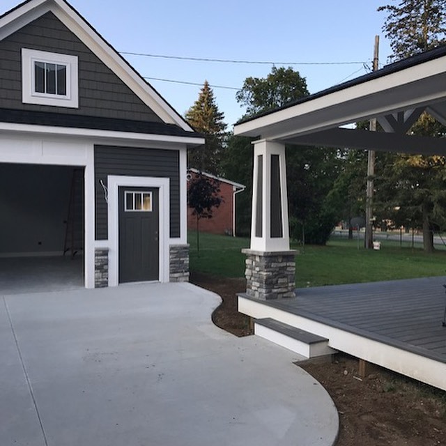 Completed deck project by QHR - LLC Roofing & Remodeling - Side view of a house with black siding on the left and a black patio area on the right separated by a concrete driveway